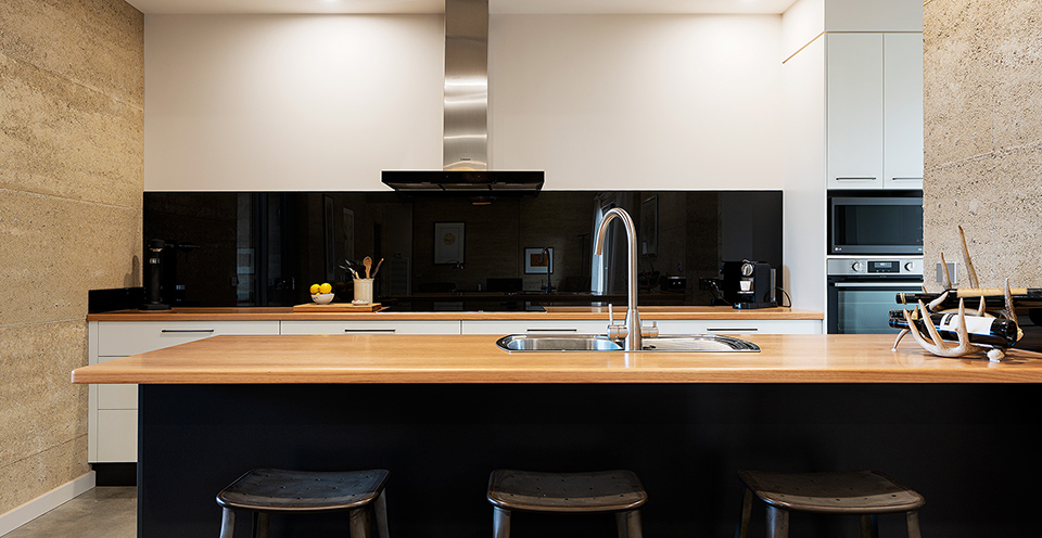 View into the kitchen showing black glass splashback and wood benchtops