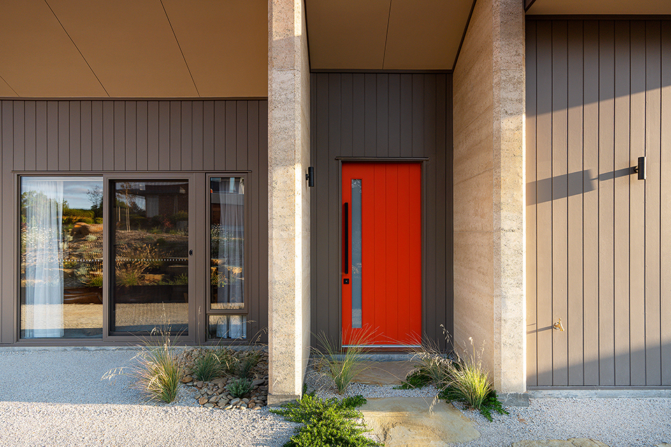 Exterior entry of the home showing large north windows into the lounge and red front door