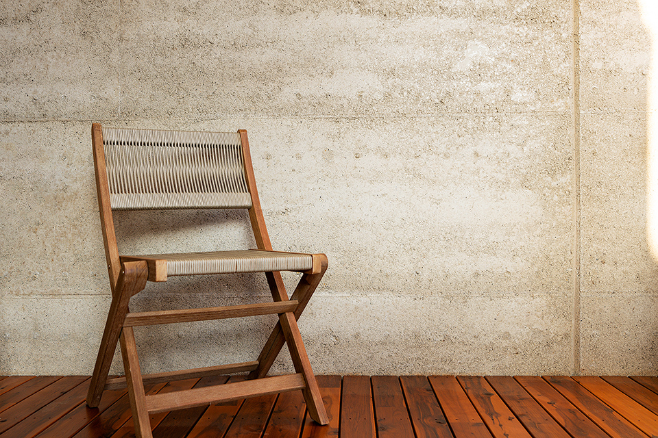 Wooden outdoor folding chair on decking with rammed earth wall behind